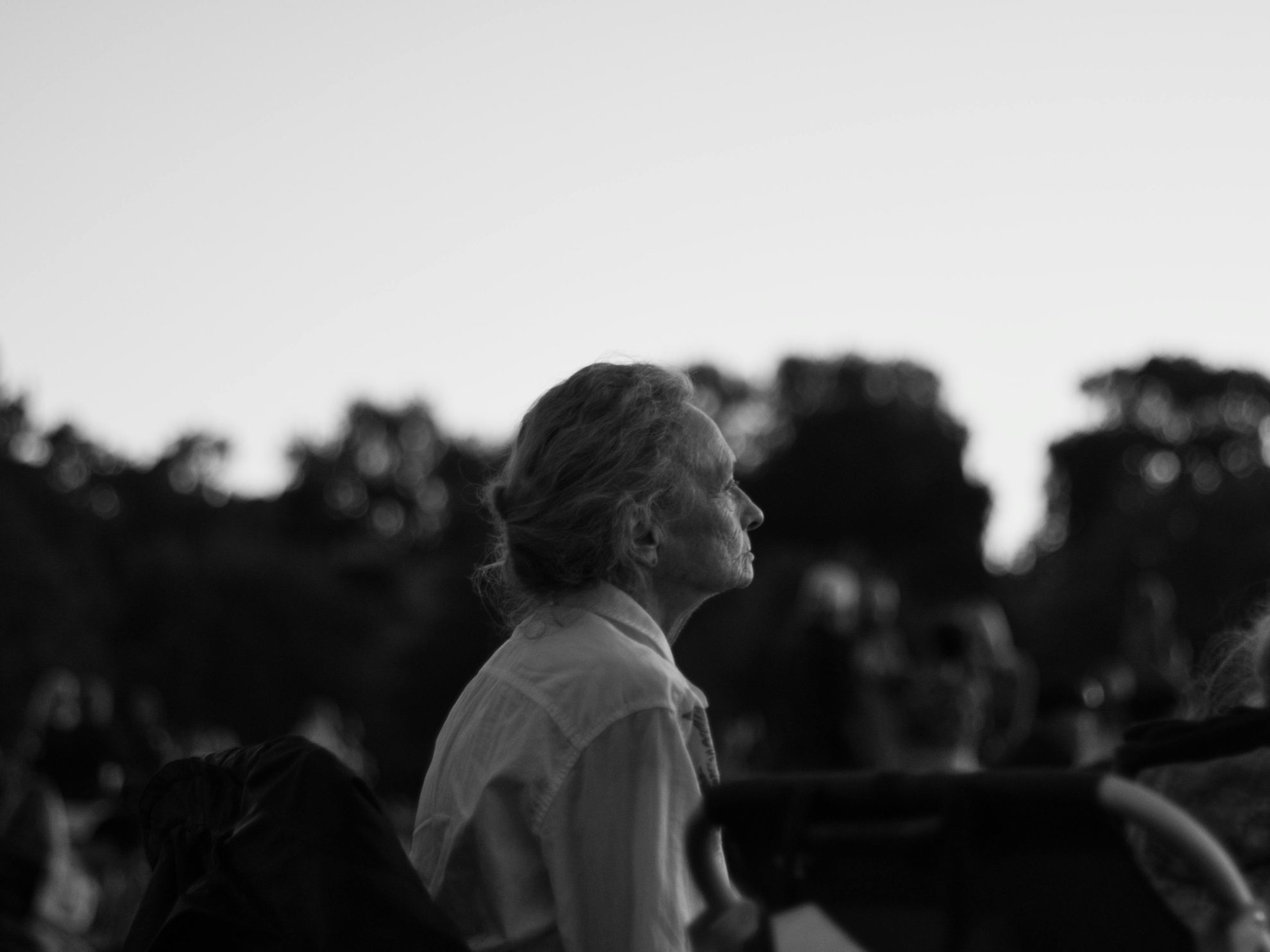 A senior woman sitting and contemplating in a park, captured in a black and white photograph.